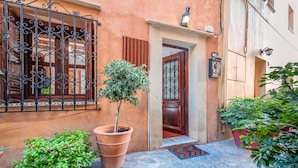 A narrow stone-paved courtyard with a potted tree, a wooden door, and a wrought iron gate. - Casa Sabbionara (Chania)
