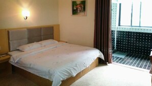 Een hotelkamer met een bed, nachtkastje, een wandlamp, een raam met gordijnen en uitzicht op een balkon.