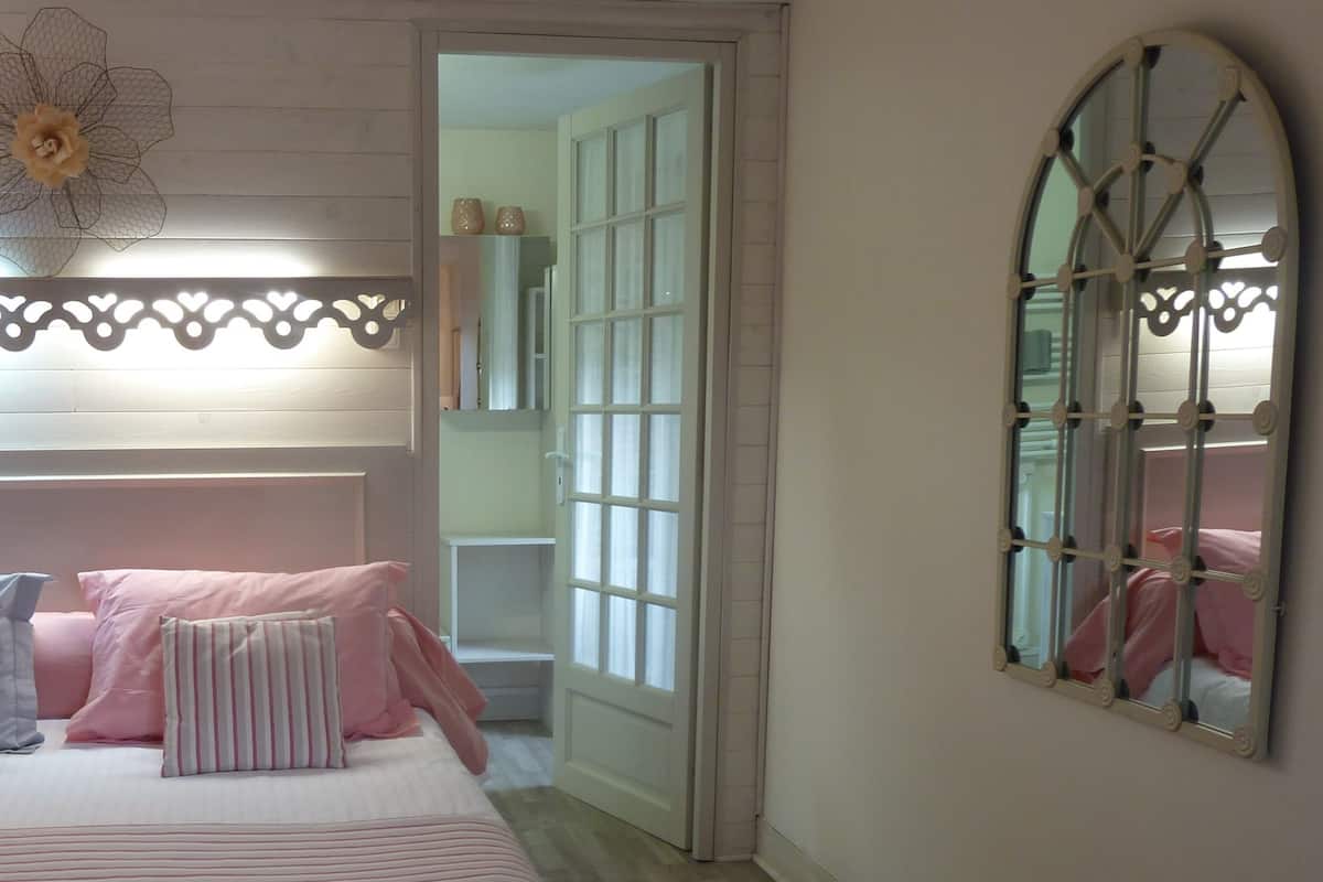 Un dormitorio con cama, almohadas, un adorno en la pared y un espejo.