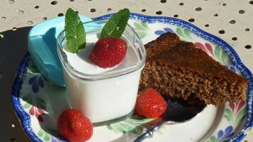 Un plato con una porción de pastel, un vaso de yogur con fresas y menta, y una cuchara.
