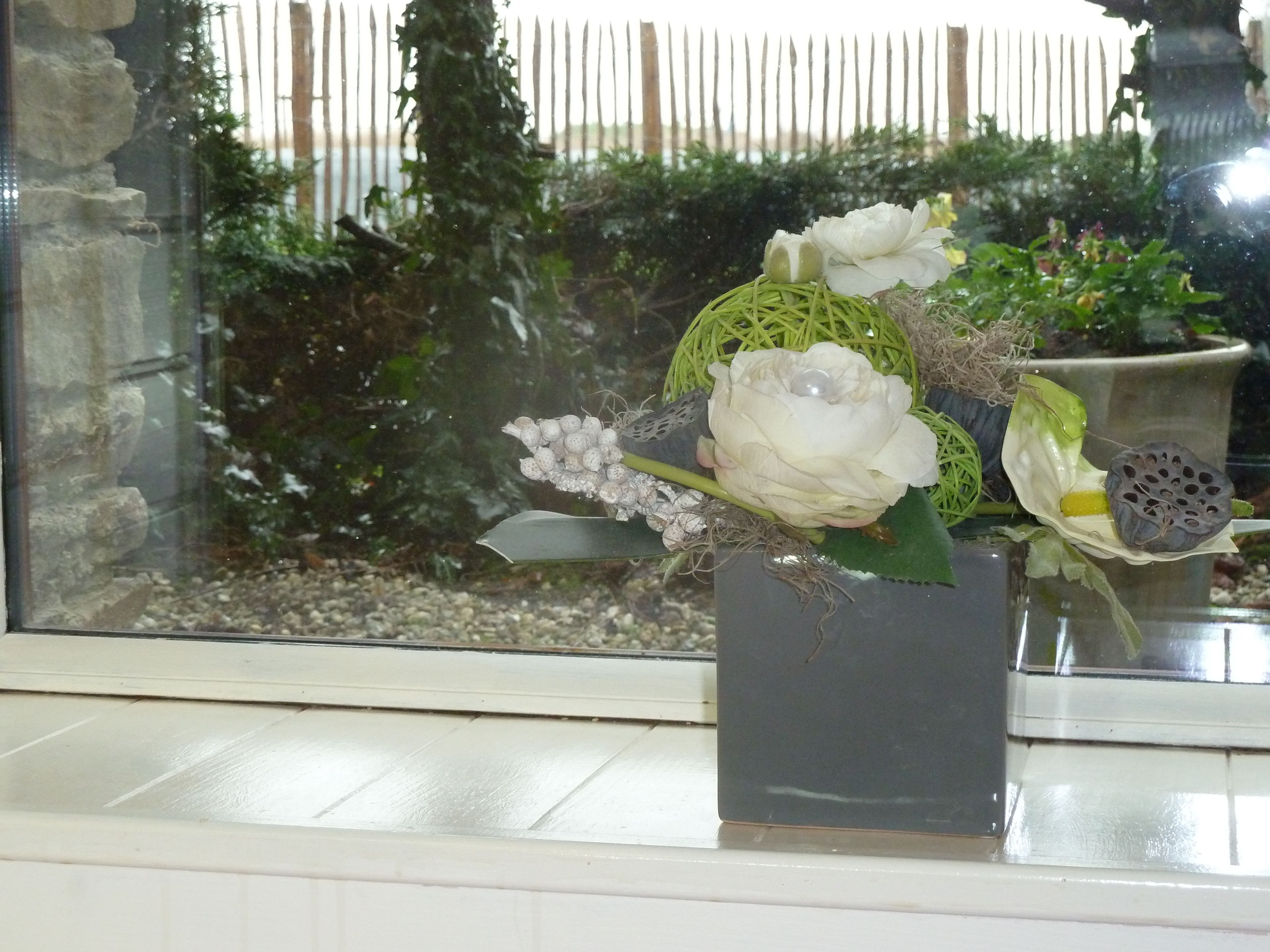 A floral arrangement in a square vase on a windowsill.