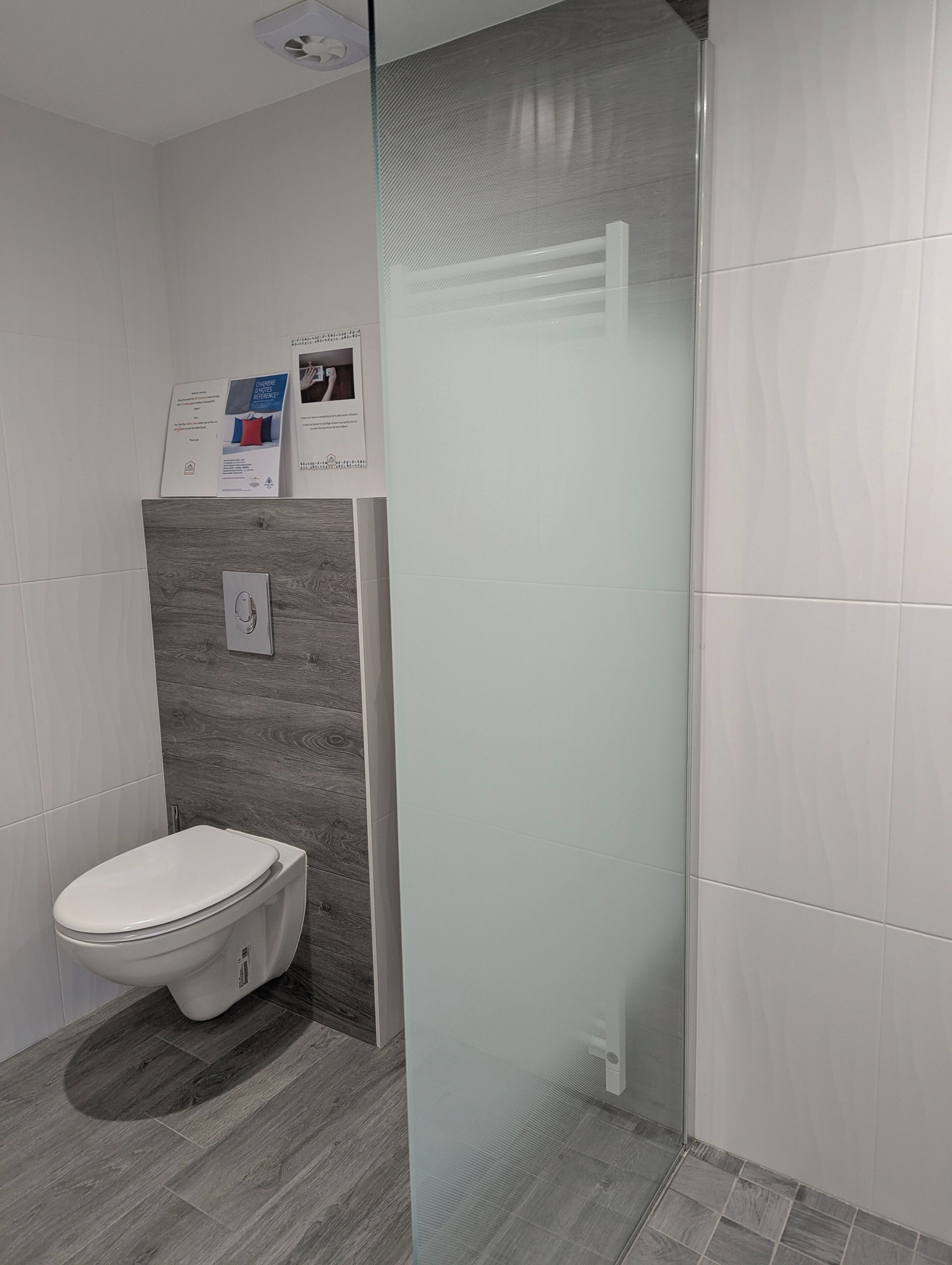 Une salle de bain moderne équipée de toilettes, d’une douche avec des portes en verre dépoli et d’un panneau de commande fixé au mur.