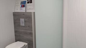 Une salle de bain moderne équipée de toilettes, d’une douche avec des portes en verre dépoli et d’un panneau de commande fixé au mur.