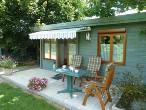 A small, cozy outdoor seating area with a table and chairs, surrounded by a garden with flowers and a wooden fence. - Les Bruyères du Mont (Ceaux)