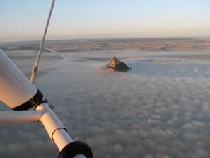 A view from an aircraft above a landscape with a prominent building on a small island surrounded by clouds. - Les Bruyères du Mont (Ceaux)