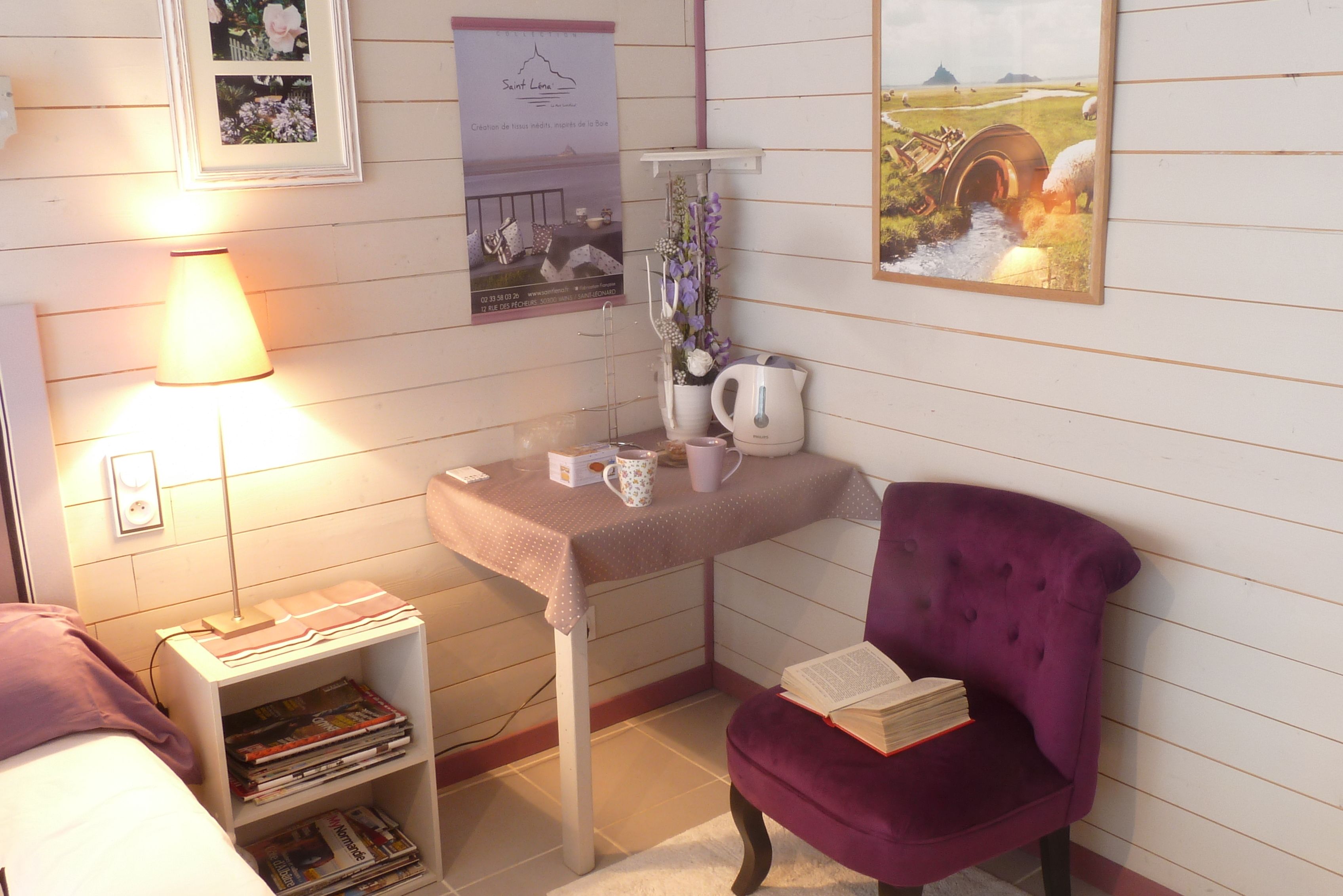 A cozy room with a bed, a desk with a lamp, a purple chair, a bookshelf, and a painting on the wall.