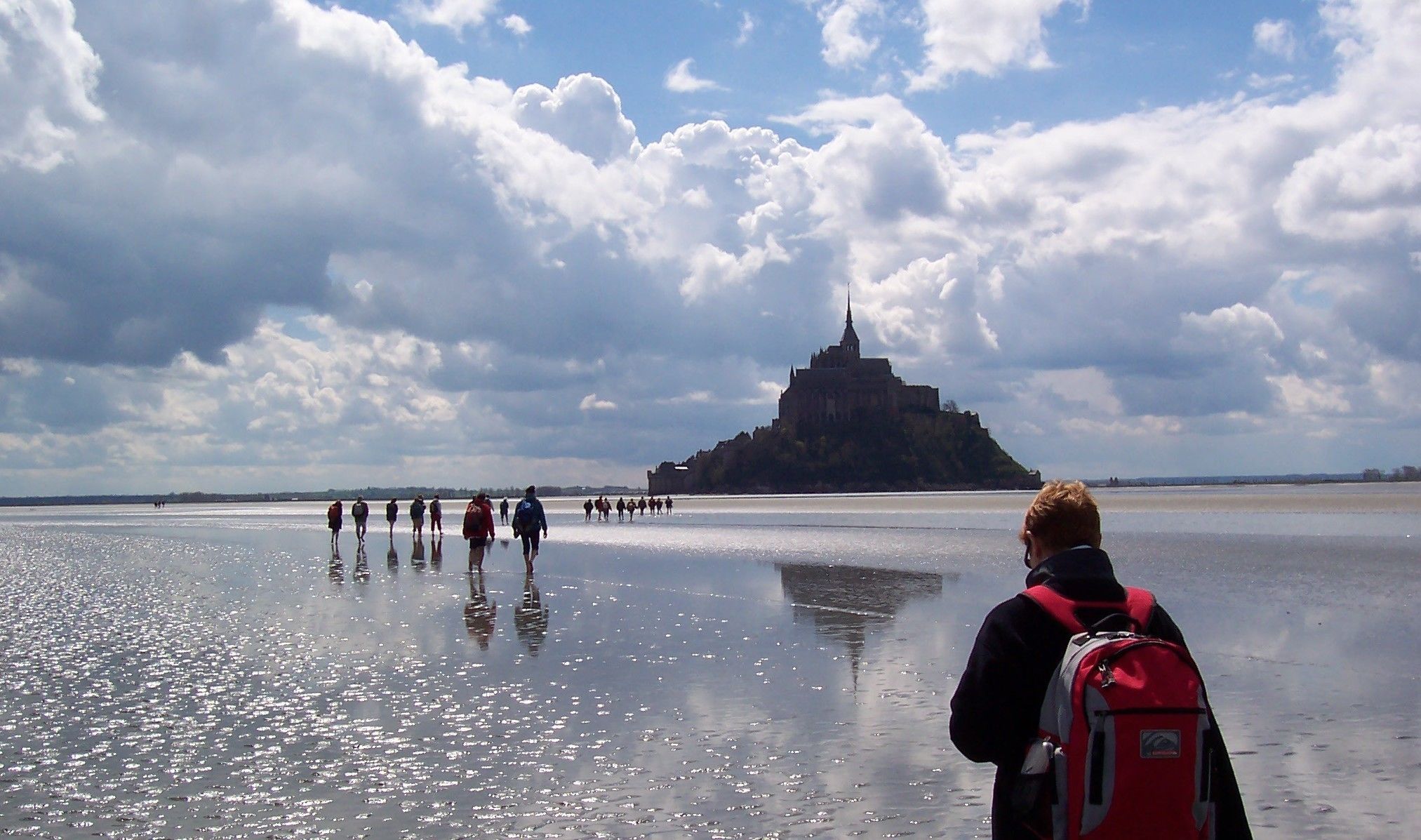 A group of people walking on a frozen body of water with a historic castle in the background.