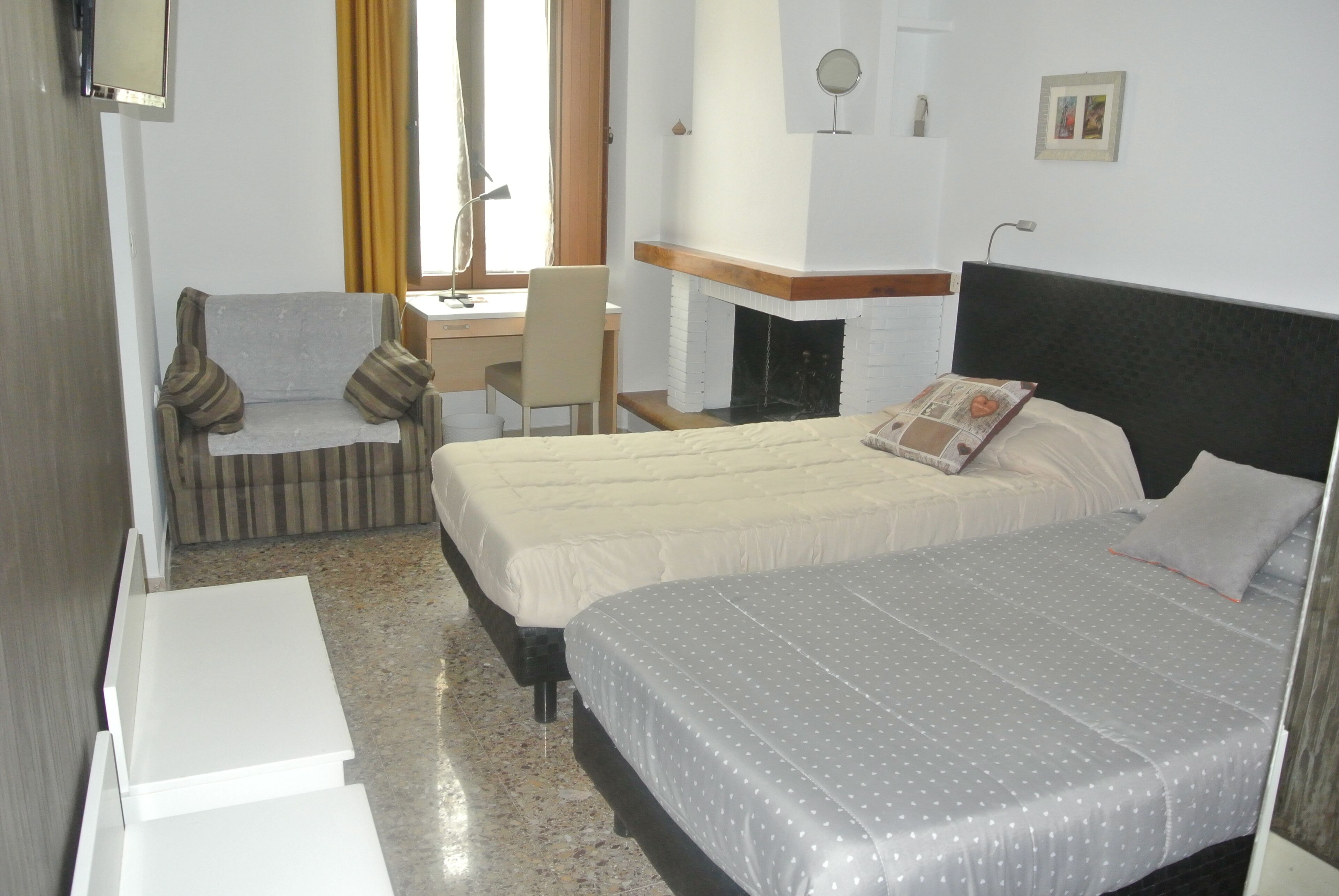 A hotel room with two beds, a desk, a chair, and a fireplace.