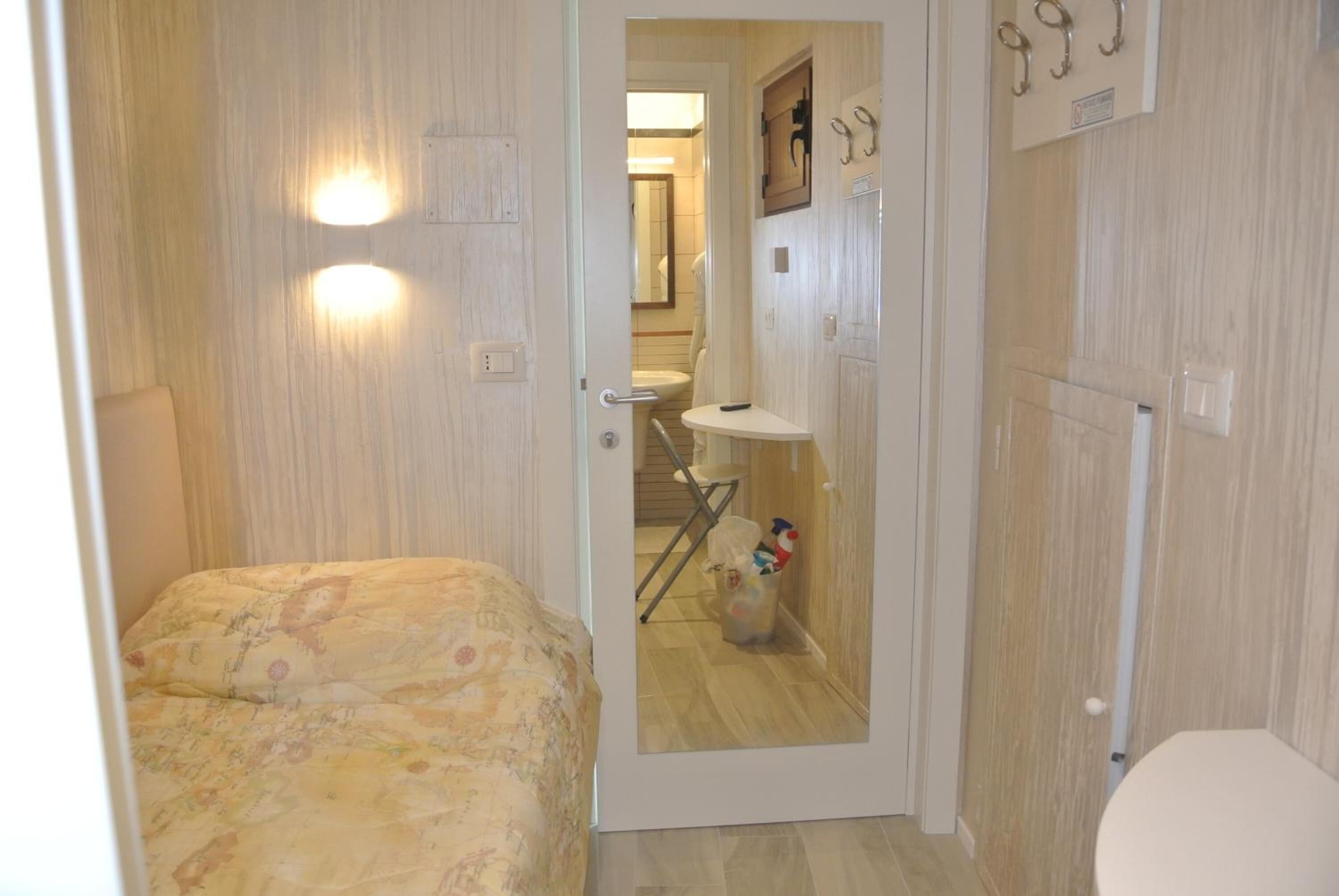 Un dormitorio con cama, un baño con lavamanos y espejo, y una puerta que da a un pasillo.