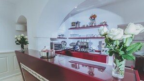 A modern kitchen with red cabinets, a marble countertop, and a coffee machine. There are white roses in a vase on the counter. - B&B Portanuova (Vasto)
