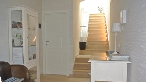 A hallway with a brown leather chair, a white desk, a staircase, and a door. - B&B Portanuova (Vasto)