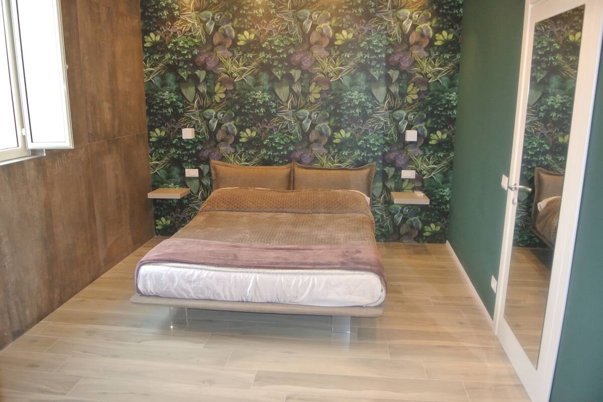 A bedroom with a bed, wooden floor, green walls, and a plant wall.