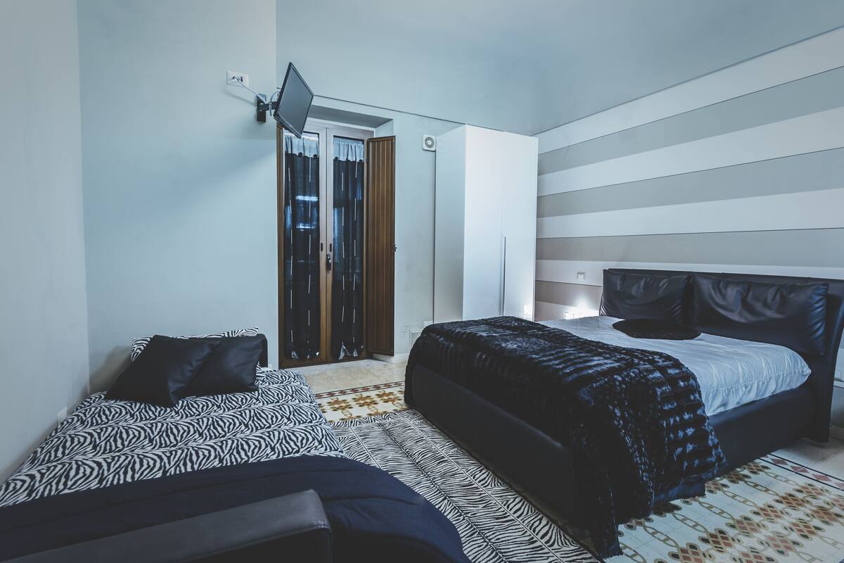 A modern bedroom with a bed, a bench, a wardrobe, and a mirror.