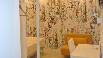 A bedroom with a floral wallpaper, a bed, a yellow sofa, and a white table.