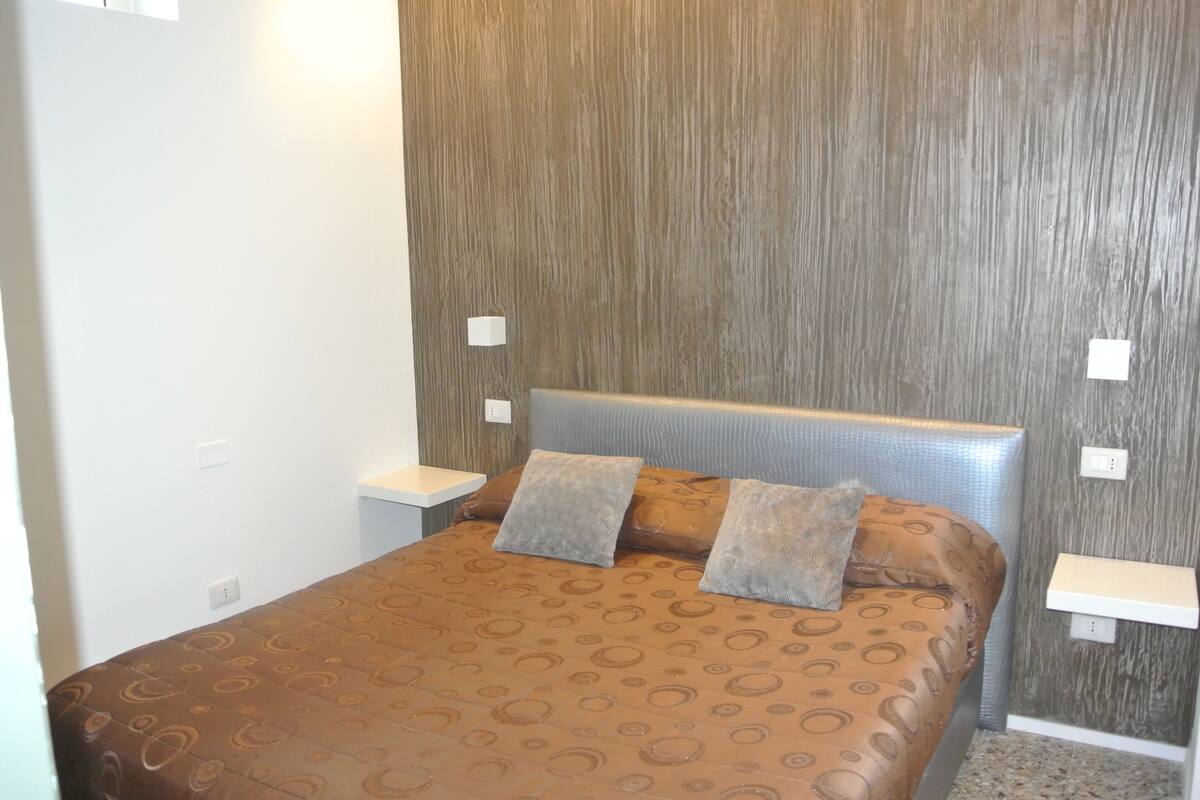 A bedroom with a brown patterned bedspread, two pillows, a headboard, and a nightstand.