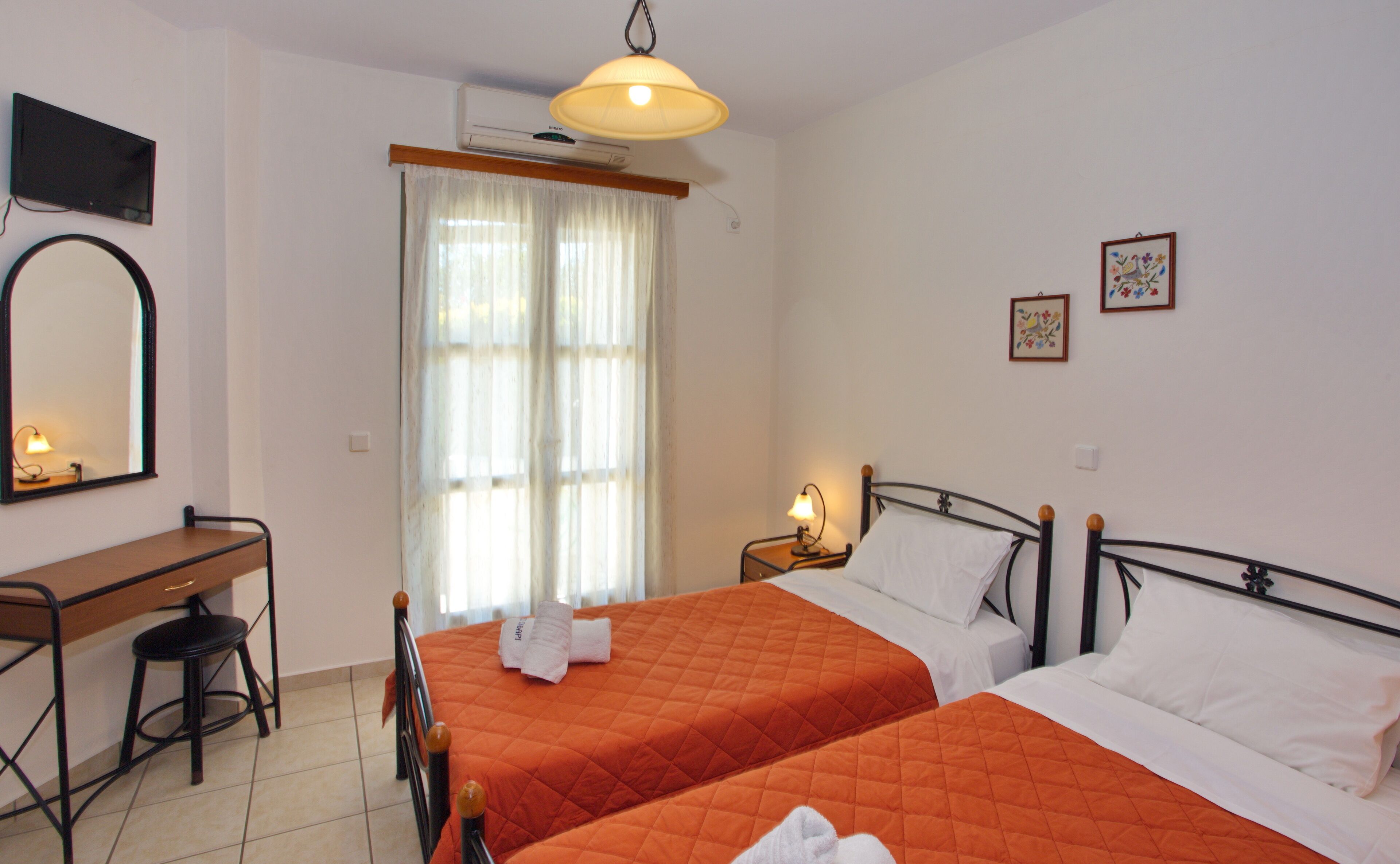 Habitación de hotel con dos camas, un escritorio con silla, un espejo y una ventana con cortinas.