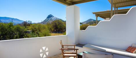 Un balcón con vistas a montañas, una silla de madera y una mesa.