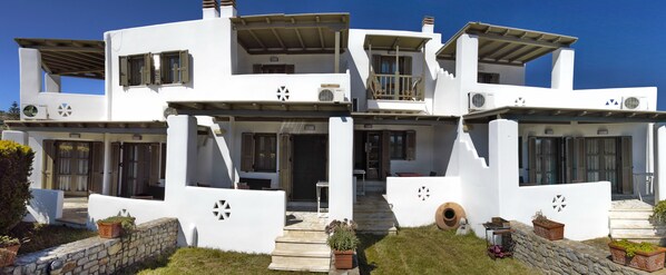 A modern white building with multiple balconies, a stone wall, and potted plants.