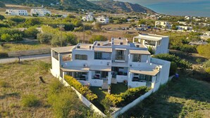 Un edificio residencial moderno de varios pisos con techo plano, rodeado de vegetación y vistas al mar.