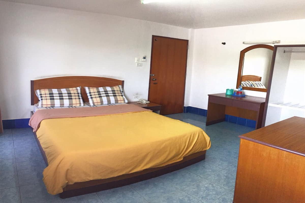 A bedroom with a bed, bedside table, dresser, mirror, and a door.