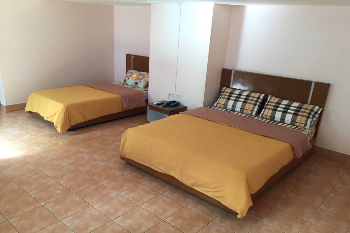 A hotel room with two beds, each with a brown bedspread, a nightstand with a phone, and a wall-mounted TV.