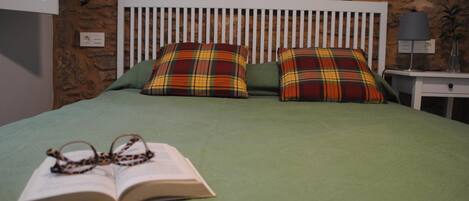 A bed with plaid pillows, a green bedspread, and an open book with glasses on it.