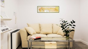 Un soggiorno con un divano beige, un tavolino in vetro, una pianta e un quadro appeso al muro.