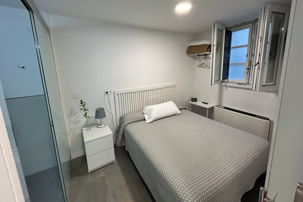 A bedroom with a bed, a nightstand, a lamp, a radiator, and a window.