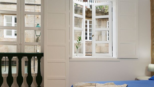 Una camera da letto con un letto, una finestra vista edifici e un balcone con ringhiera.