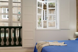 A bedroom with a bed, a window with a view of buildings, and a balcony with a railing. - Pensión Rua Nova (Santiago de Compostela)