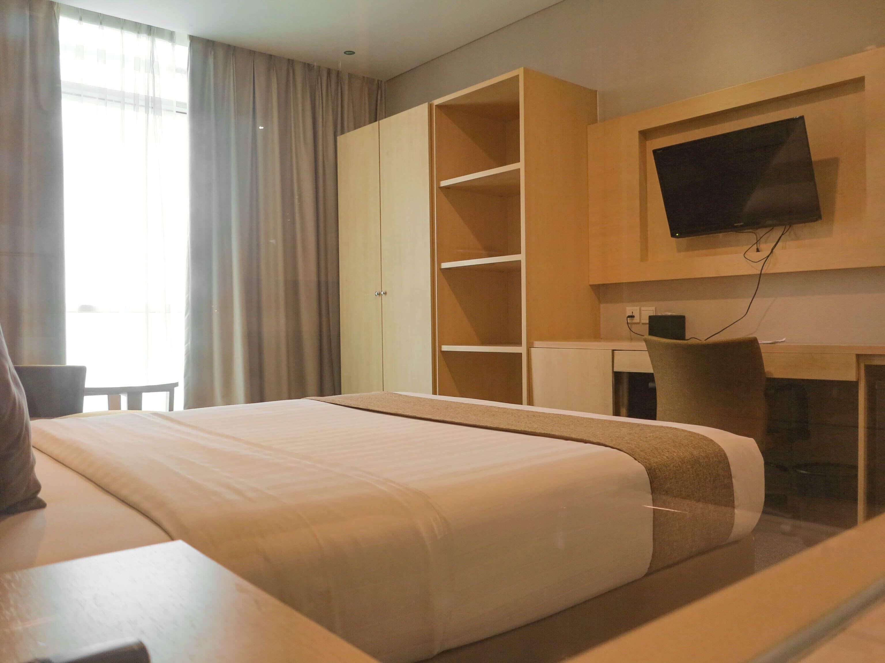 Una camera d'albergo con un letto, una scrivania, una sedia, una televisione e un armadio.
