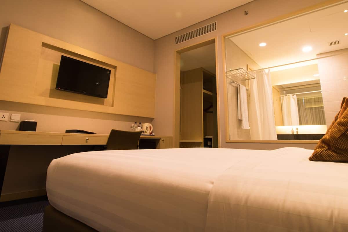 Una habitación de hotel con una cama, un escritorio con silla, un televisor y un espejo grande.