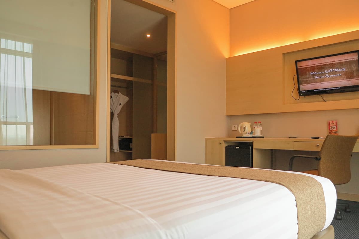 Una habitación de hotel con cama, escritorio, silla, televisor y armario.
