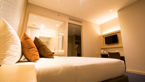 A hotel room with a bed, pillows, a TV, a desk with a chair, and a wardrobe. - GTV Hotel & Service Apartment (Cikarang)