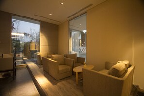 A modern living room with sofas and a coffee table, large windows, and a view of the outside. - GTV Hotel & Service Apartment (Cikarang)