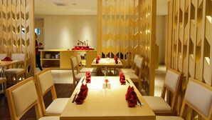 A restaurant with wooden furniture and a modern design, featuring tables set with red napkins and cutlery. - GTV Hotel & Service Apartment (Cikarang)