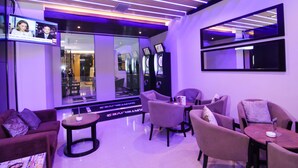 A modern lounge area with purple lighting, comfortable seating, and a large mirror. - GTV Hotel & Service Apartment (Cikarang)