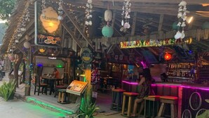 Un espace bar extérieur aménagé avec du mobilier en bois, des néons et des décorations suspendues.