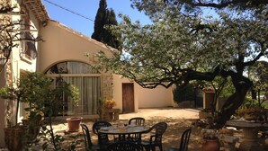 A courtyard with a round table and chairs, surrounded by potted plants and a building with a wooden door. - Holiday Home in Provence with Pool & Tennis (Piolenc)