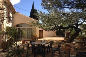 A courtyard with a table and chairs, surrounded by potted plants and a building with a tiled roof.