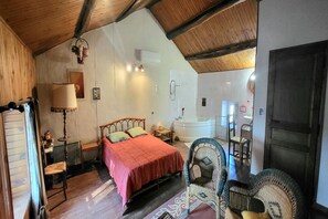 A bedroom with a bed, bedside table, lamp, and a bathroom with a bathtub and sink.