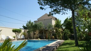 A swimming pool with lounge chairs, a building with a sloped roof, and surrounding greenery. - Holiday Home in Provence with Pool & Tennis (Piolenc)
