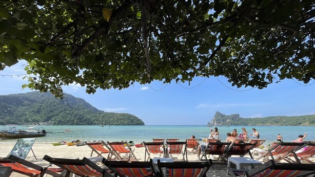 A beach with rows of striped beach chairs and umbrellas, a clear view of the sea, and boats in the water. - Twin Palms Hostel Phi Phi (Ko Phi Phi)
