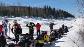 A group of snowmobiles lined up on a snowy path with trees in the background.