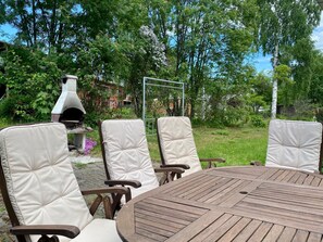An outdoor seating area with a round wooden table and four cushioned chairs. - Villa Prud (Kuopio)