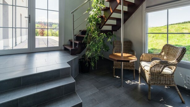 A modern staircase with a glass door leading to a balcony, wicker chairs, and a view of a green landscape. - Group Escape in Mellier (Mellier)