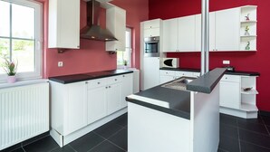 A modern kitchen with white cabinets, a central island, and a red accent wall. - Group Escape in Mellier (Mellier)