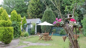 A garden with a stone pathway, a wooden table and chairs, and a birdhouse. - Remarc House Stansted (Bishop's Stortford)