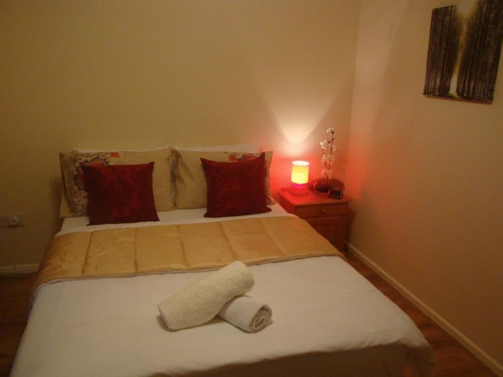 Una cama bien hecha con una toalla enrollada, una mesita de noche con una lámpara y una obra de arte en la pared.