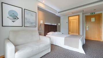 Ein Hotelzimmer mit einer Couch, zwei Betten, einem Kopfteil und gerahmten Kunstwerken an der Wand.